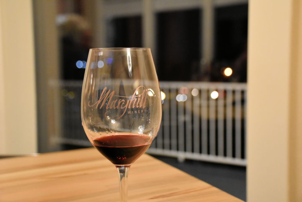 glass of red wine from maryhill winery sitting on a wood table at night