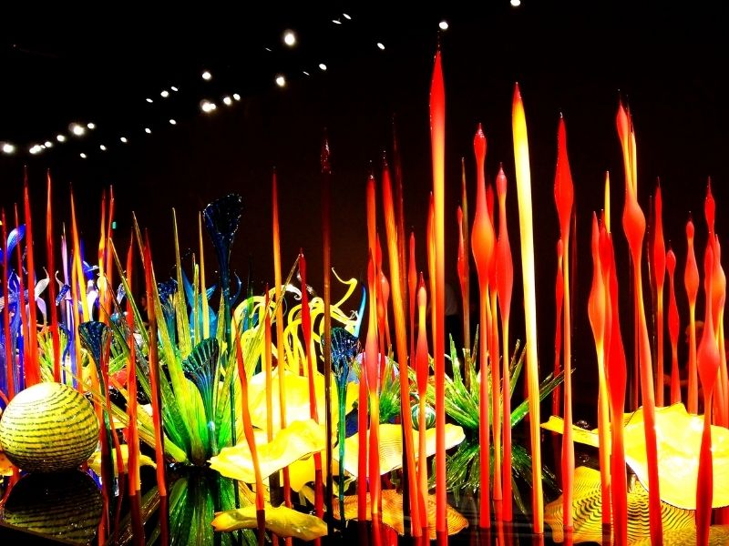 Red and yellow and green blown glass sculptures forming what looks to be a garden. Glass art by Dale Chihuly shown in a museum in Seattle in winter.