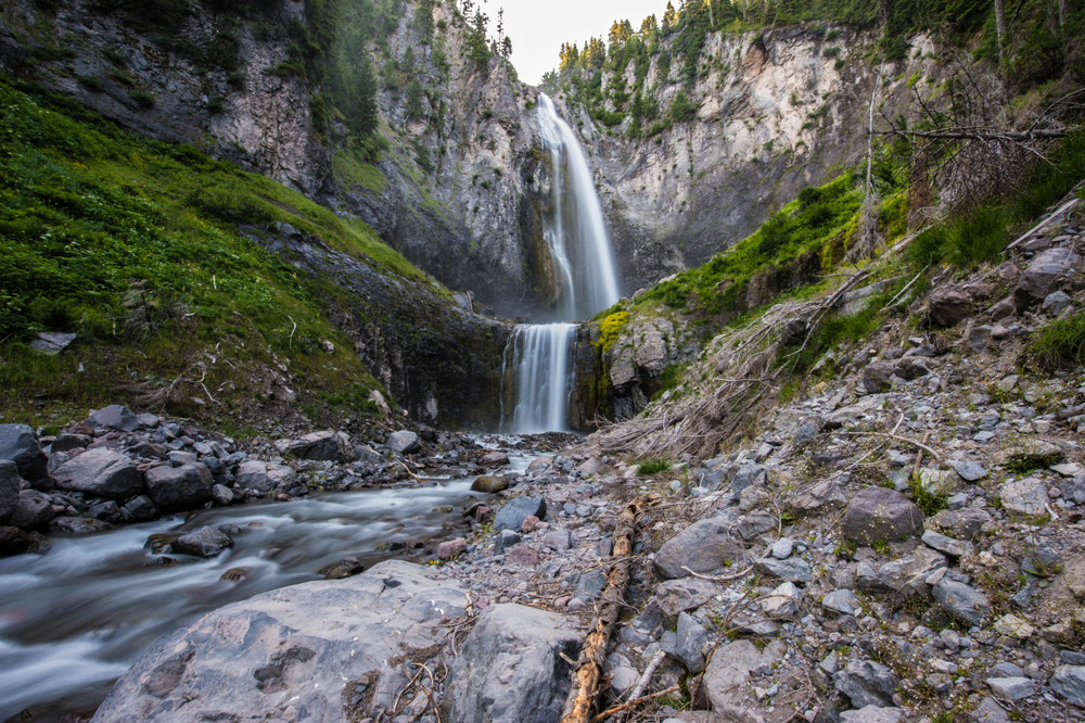 A low angle view of a two-tiered Washington State waterfall in Mount Rainier National Park, with rocks and grass in the foreground.
