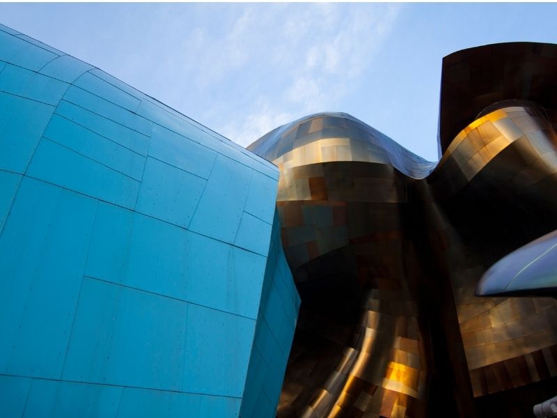 Close up of modernist architecture at the Museum of Popular Culture: one side is curved and teal, the other is bronze and curved architectural pieces in traditional Frank Gehry style.