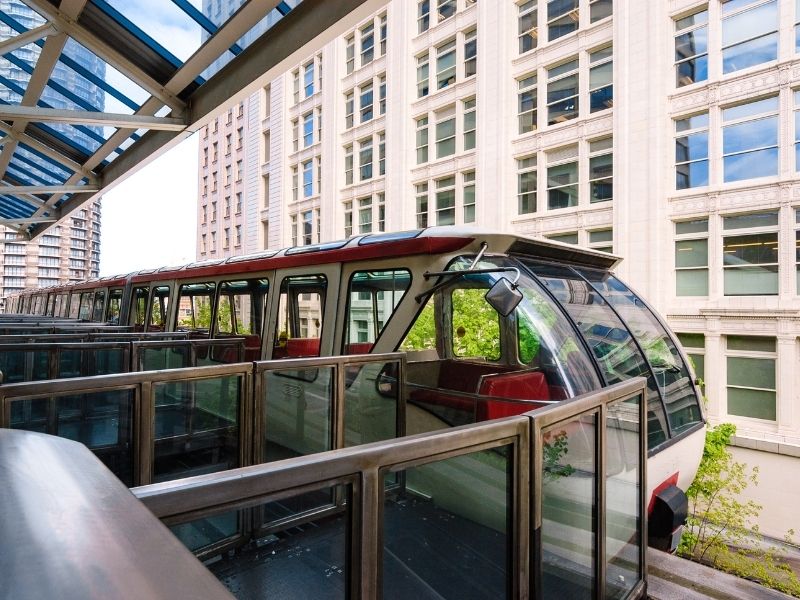 White and red Seattle monorail car pulling into a station at Seattle Center with a white building in the background.