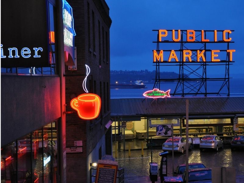 Night view of Pike Place Market with neon sign saying "Public Market" and a neon sign of a cup of coffee.