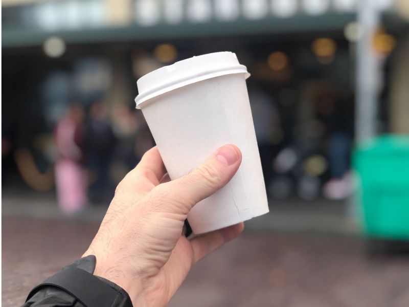 Hand holding a white coffee cup with a blurred out background.