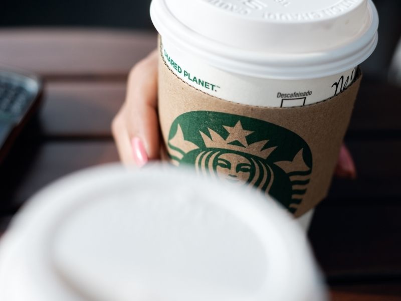 Two Starbucks cups cheersing with focus on the logo on the paper cup.