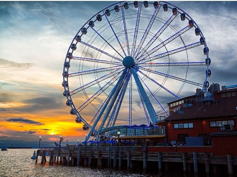 The Seattle Great Wheel giant Ferris Wheel on the pier at sunset with a cloudy sky featuring brilliant colors.