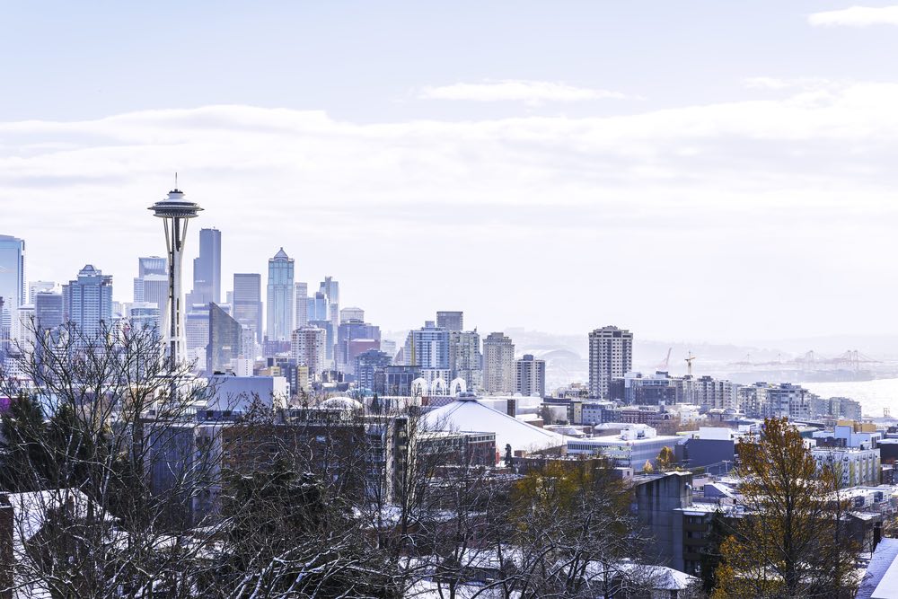 A snow covered Seattle cityscape on a lightly cloudy day with a bit of pale blue sky showing on a winter day.