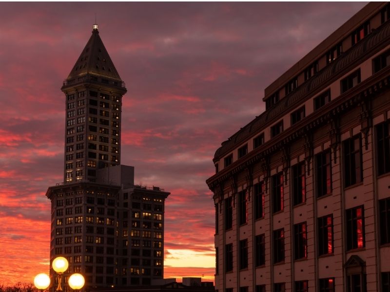 Orange and pink sunset colors of the Smith Tower Observation Deck, one of the tallest skyscrapers in Seattle at one point, and another building in the foreground.