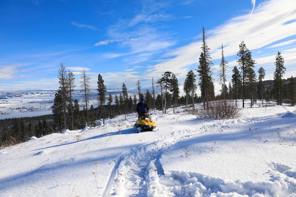 A  man on a yellow snowmobile in the Cascade mountains on a sunny day with lots of snow