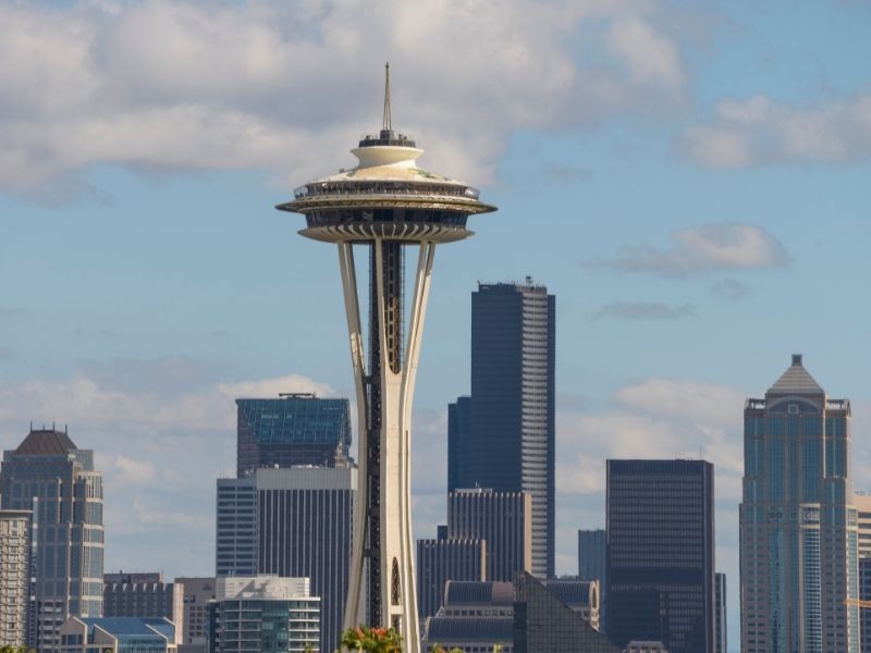 A photo of the iconic Space Needle Observation Deck with other Seattle skyscrapers in the background on a partly cloudy day. Going up the Observation deck is a Seattle bucket list must.