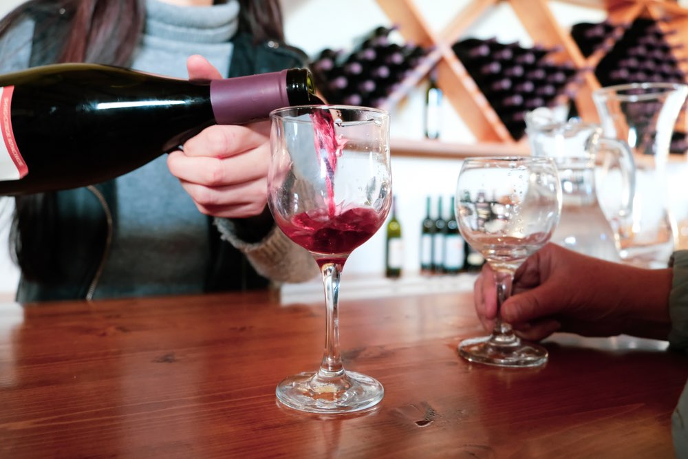 Tasting room sommelier pouring a glass of red wine for a client visiting the establishment.