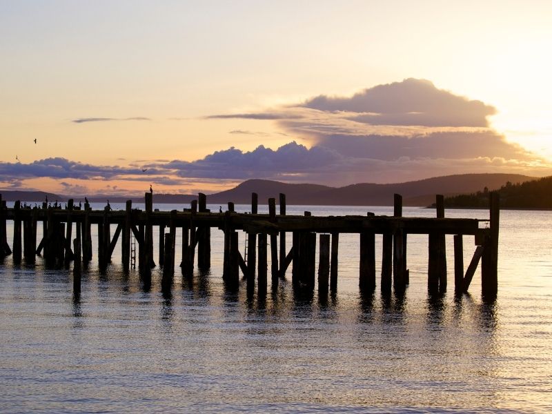 Wooden pier at sunset with a orange and pink cloudy sky reflecting onto the water