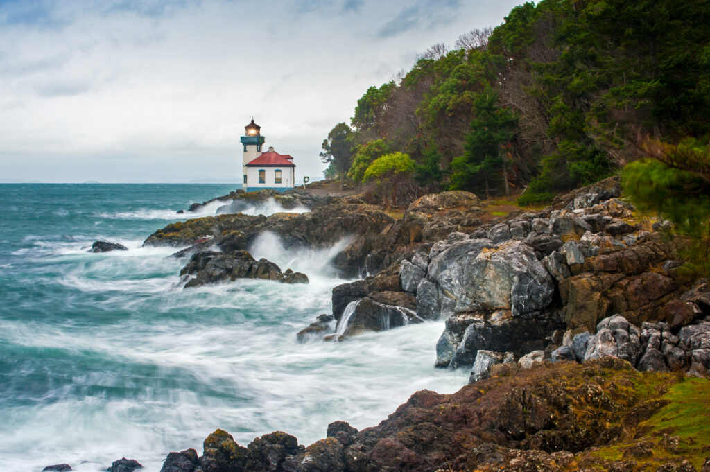 rocky coastline with lighthouse in the distance as seen in friday harbor washington state