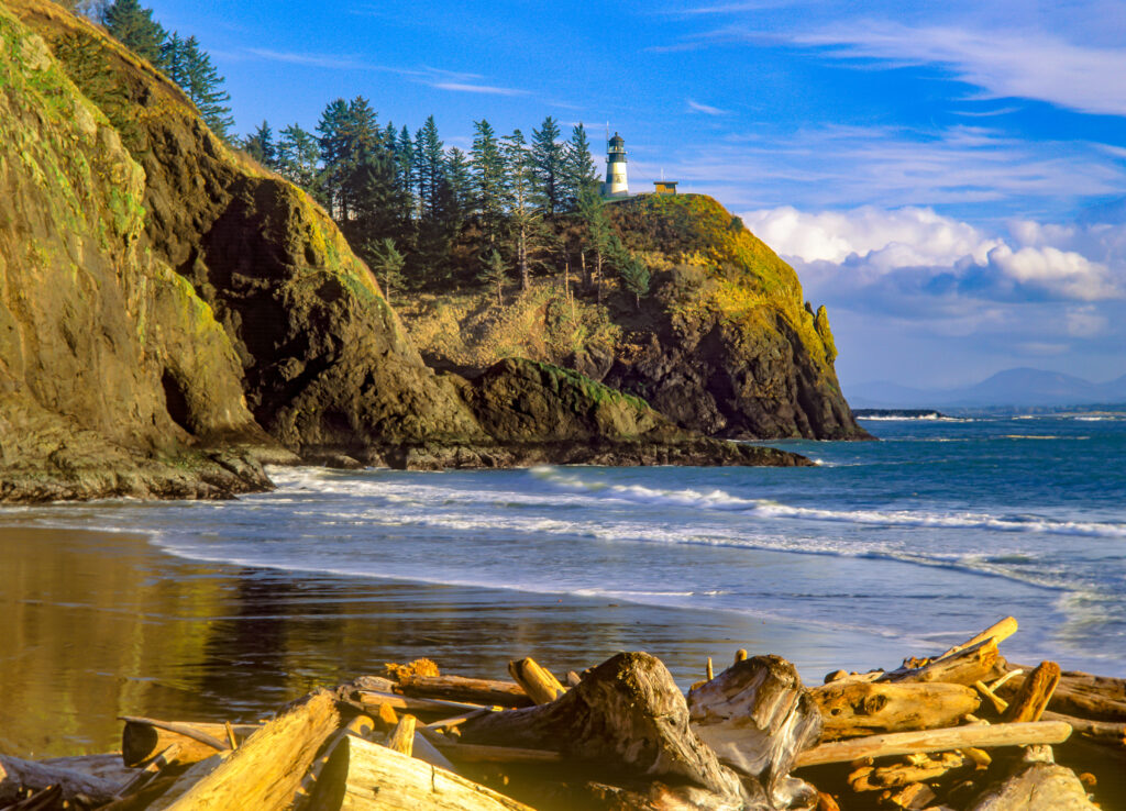 beach at cape disappointment, home to some of the best washington state beaches. a lighthouse is visible on a cliff in the distance