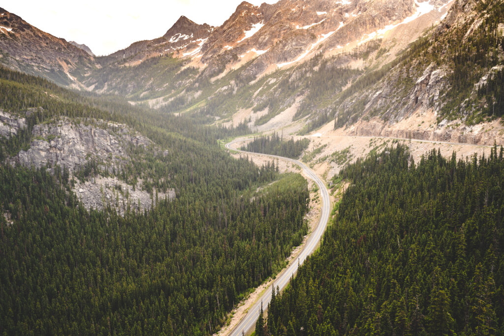 view of Cascades Lakes National Scenic Byway from above on a cloudy day with a forest visible below and mountains ahead