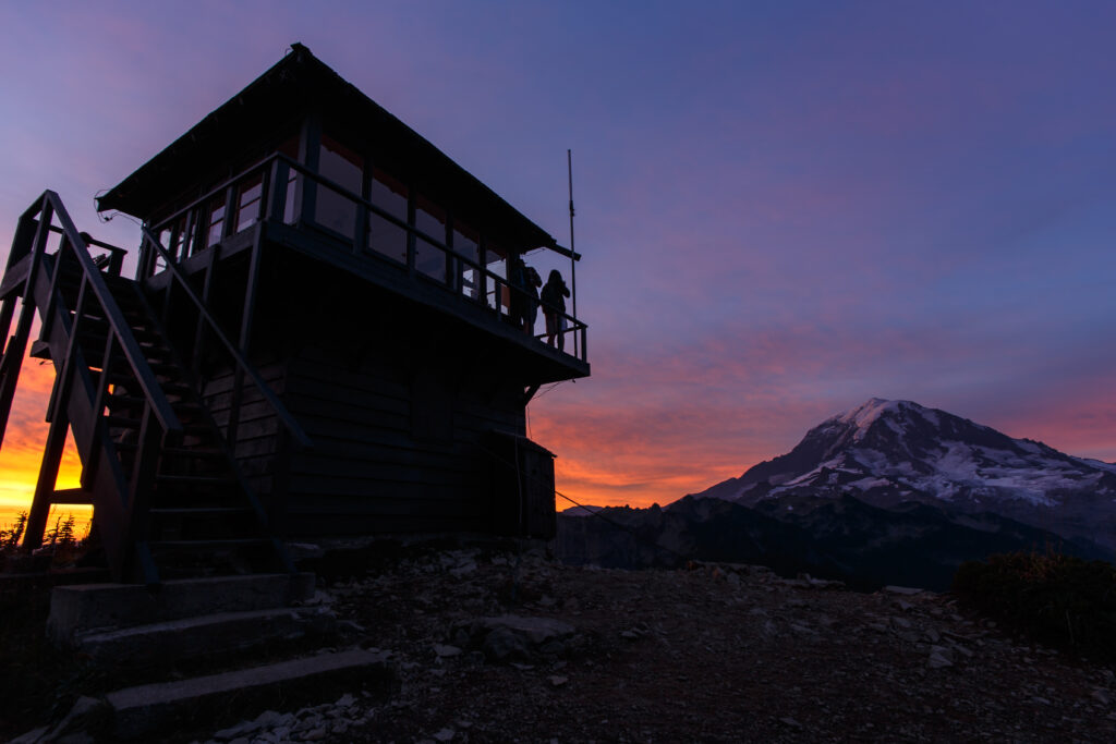 tolmie peak lookout stand in mount rainier national park at sunset. serveral people are standing nearby taking photos