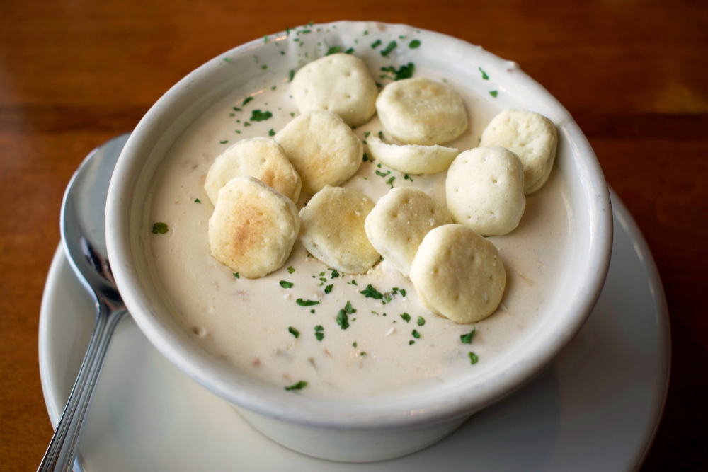 Hearty bowl of clam chowder with parsley and round oyster crackers on top, served at a restaurant. A Seattle winter favorite.