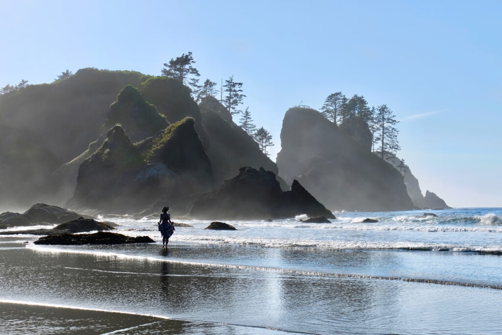 woman walking along a beach in washington with haystacks ahead of her