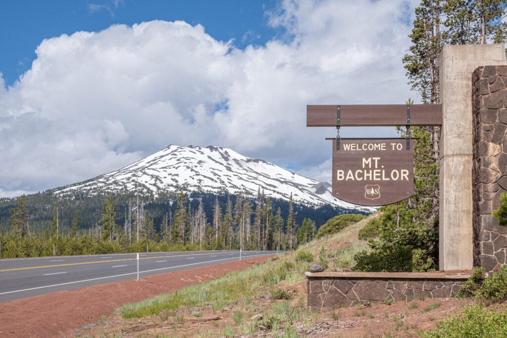 view of snowcapped mount bachelor with a wood sign saying "welcome to mt bachelor" in the foreground