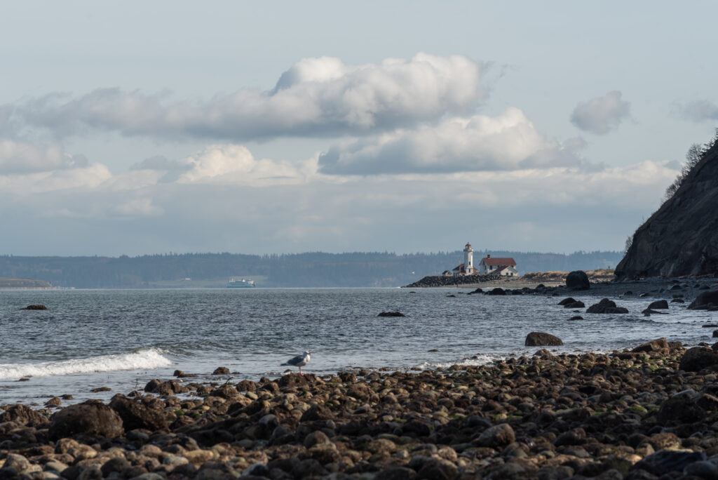 rocky beach with a lighthouse in the distance at fort worden state park, one of the best weekend getaways from seattle washington