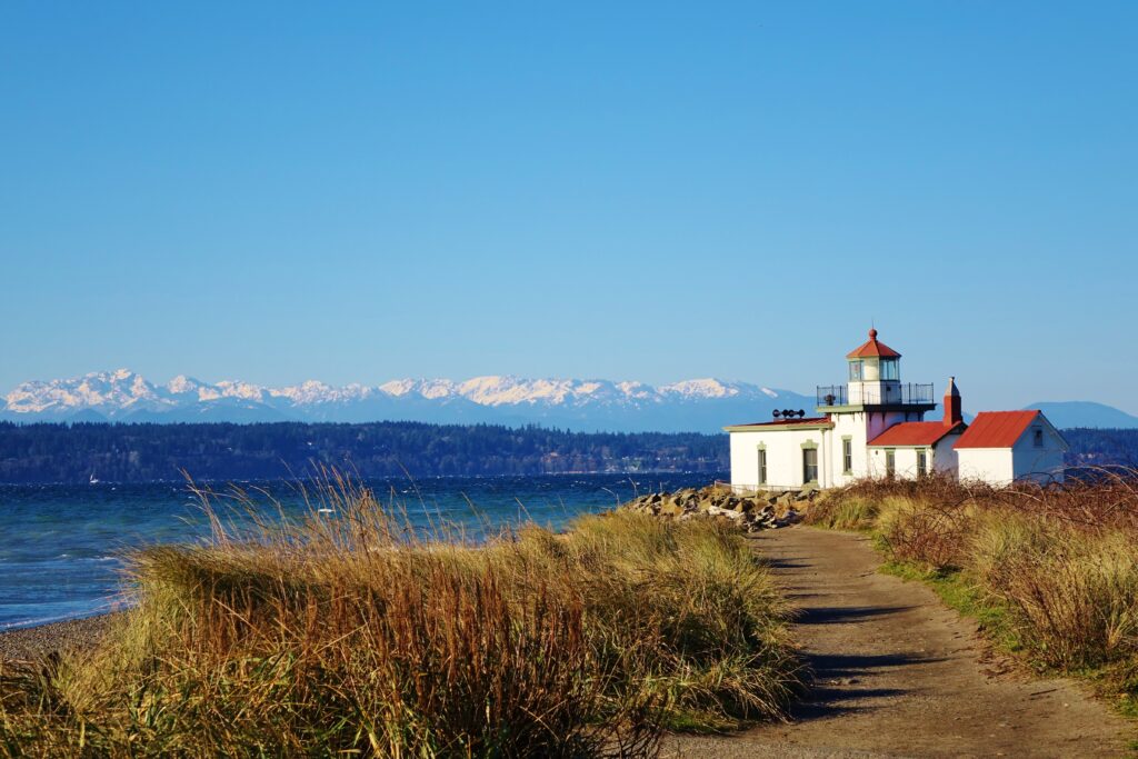 view of the lighthouse at discovery park, one of the best hikes near seattle wa. the view is from the trail with mountains visible in the distance