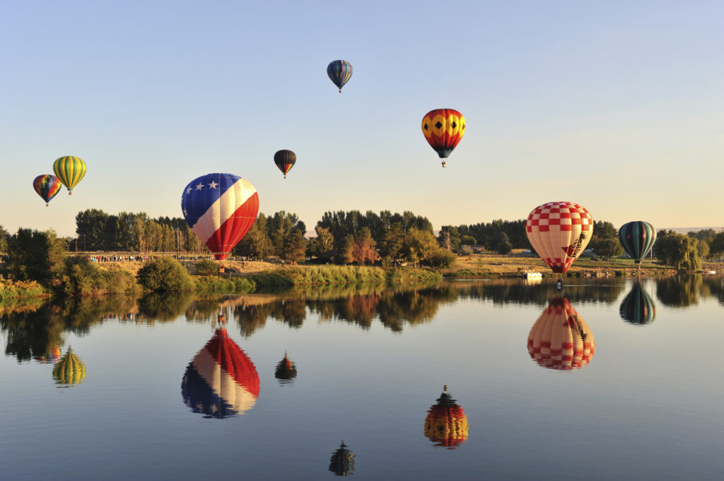 hot air balloons rising over a lake in prosser washington and reflecting into the water below