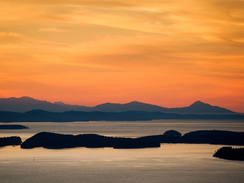 A sunset photograph of the San Juan Islands in Washington State with bright orange sky and shadowed islands.