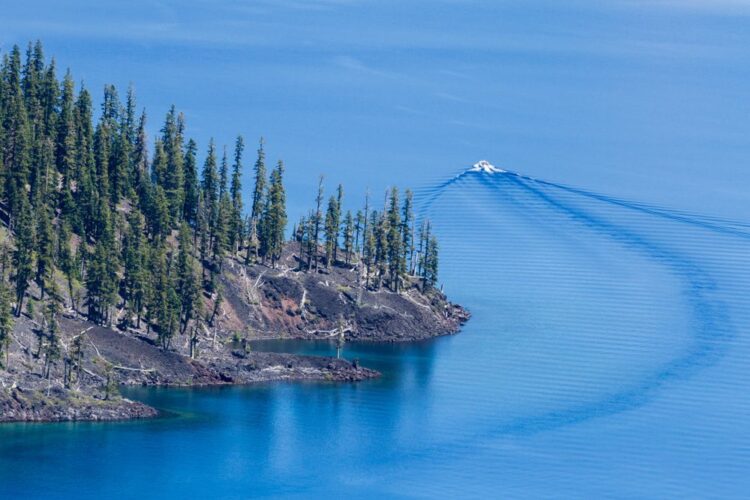 A boat passing by the edge of Wizard Island, a tree-covered small island, in Crater Lake.