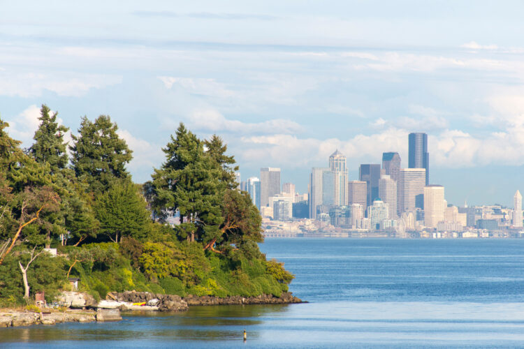 View of the Seattle skyline with an island in front of it from the water on a ferry on a partly cloudy day.