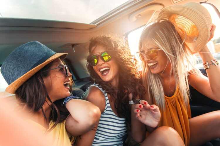 group of young women laughing in the backseat of a car on a road trip