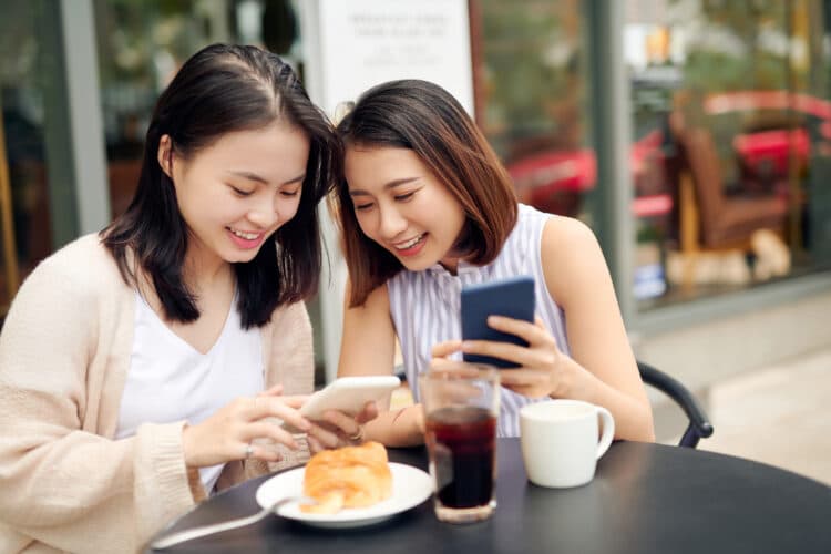 two young women sitting at a black patio table looking at their cell phones and drinking coffee bend oregon