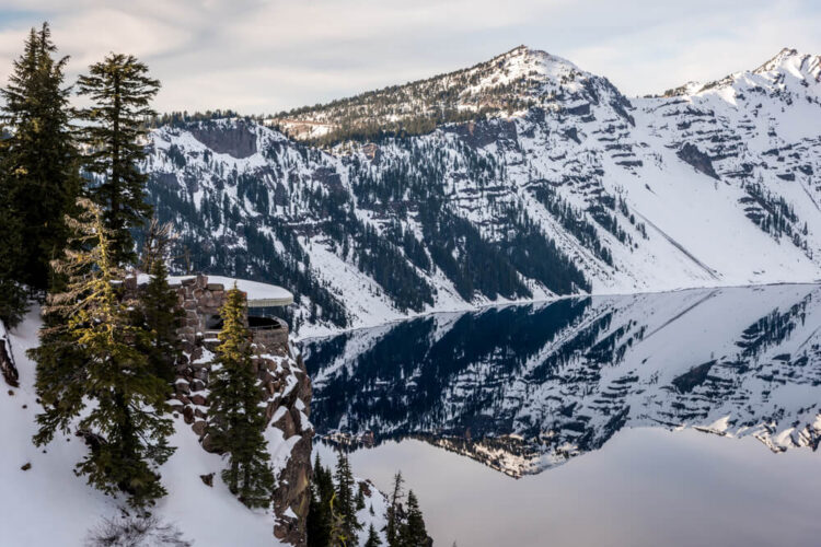 View of the mirror effect of Crater Lake as it reflects a snow-covered mountain with soft morning light from an overlook in the park