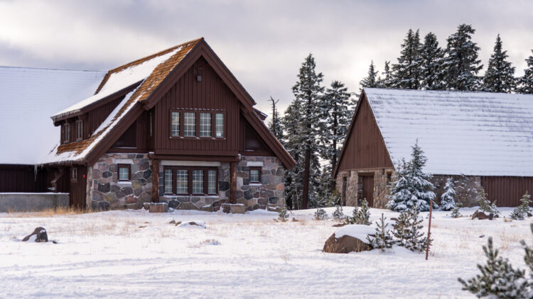 View of stone and wood buildings covered in snow, in a snowy landscape in Crater Lake in winter by the visitor center.