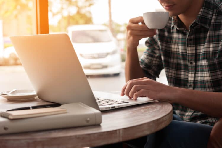 man at a laptop wearing a flannel shirt sipping from a white mug