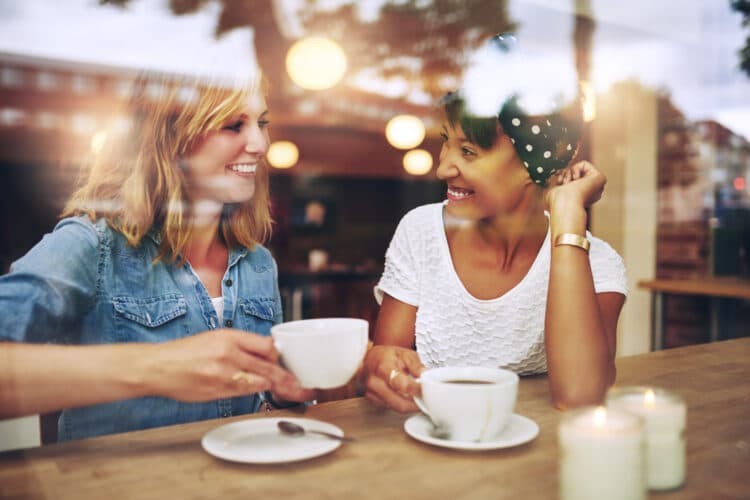 two women sitting at a wooden table in a coffee shop as shot through a window