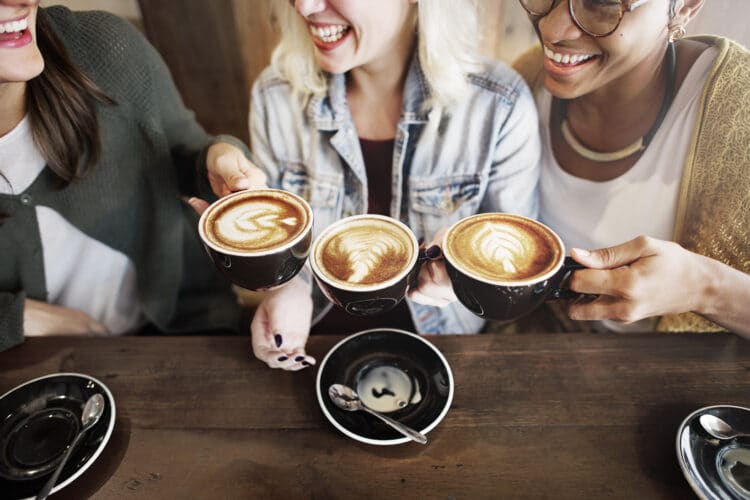 3 friends holding up lattes at one of the best places to get coffee in bend or