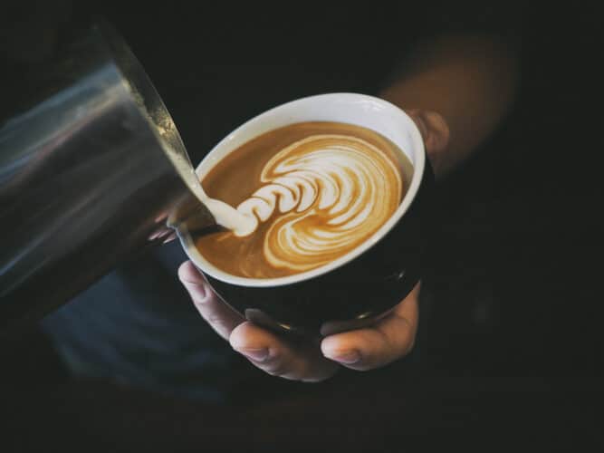 hand of a barista pouring steamed milk into a latte