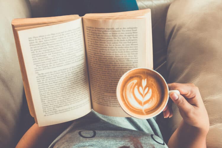 woman in a  plush armchair holding an open book and a latte