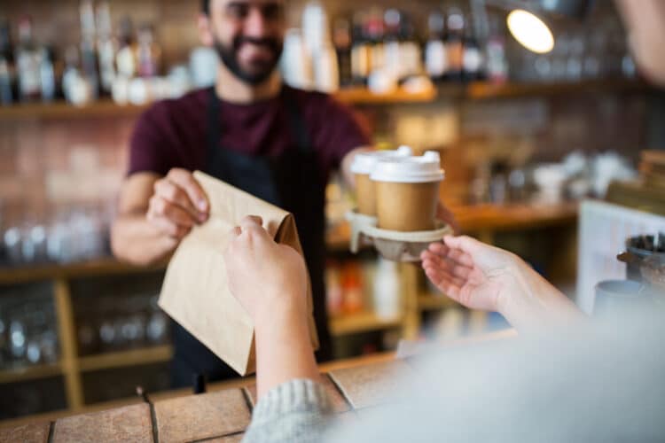 barista handing over coffee and a brown bag with pastry to go