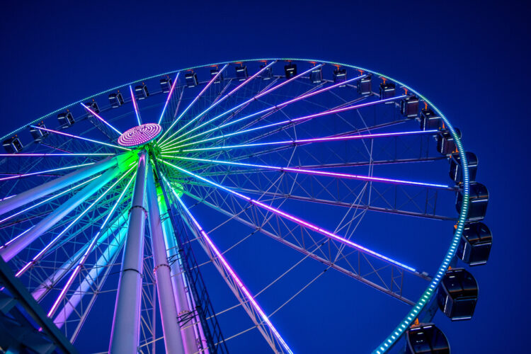 A low-angle shot looking up at the neon pink, blue, and green lights of the Great Wheel (Ferris Wheel) in Seattle.