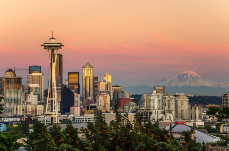 An orange and pink sunset seen from Kerry Park with the Space Needle and Mt Rainier covered in snow off in the distance.