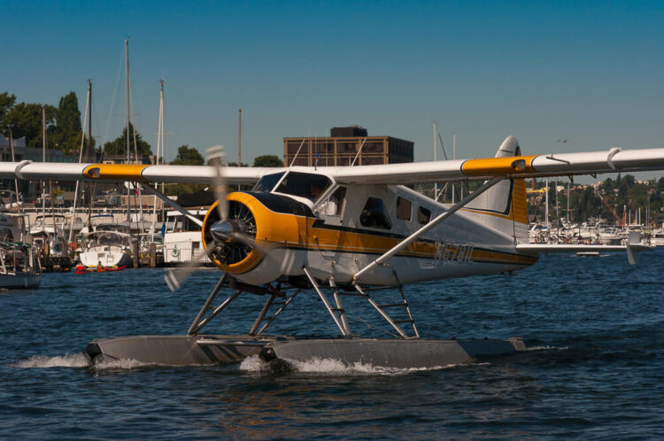 A yellow and white seaplane landing on the water on two small pontoons