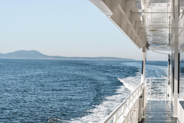 View from a whale watching boat towards the back of the boat, mountains in the distance, on a clear day in Seattle