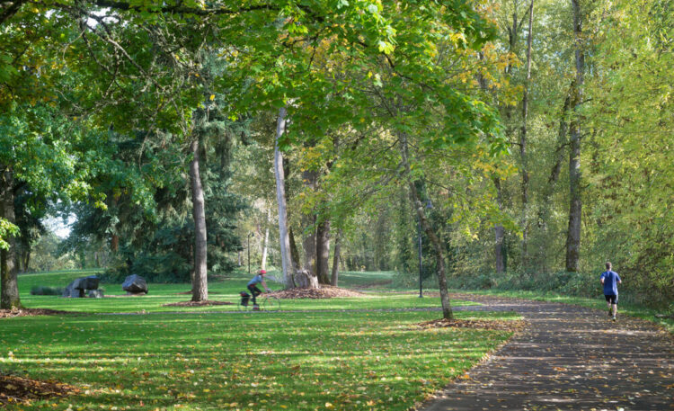 One person running and one person on a bike on a path in the green park Alton Baker Park in Eugene Oregon. This is a popular thing to do in Eugene!