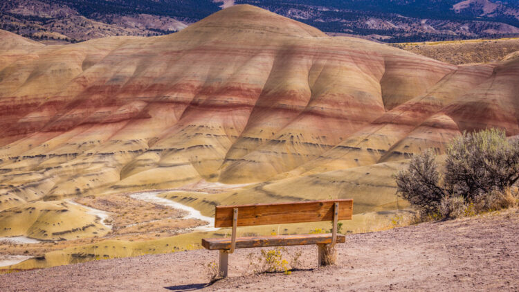 Wooden bench on a background of yellow-red mountains. Beautiful view of the CARROLL RIM TRAIL, Painted Hills, Oregon, USA