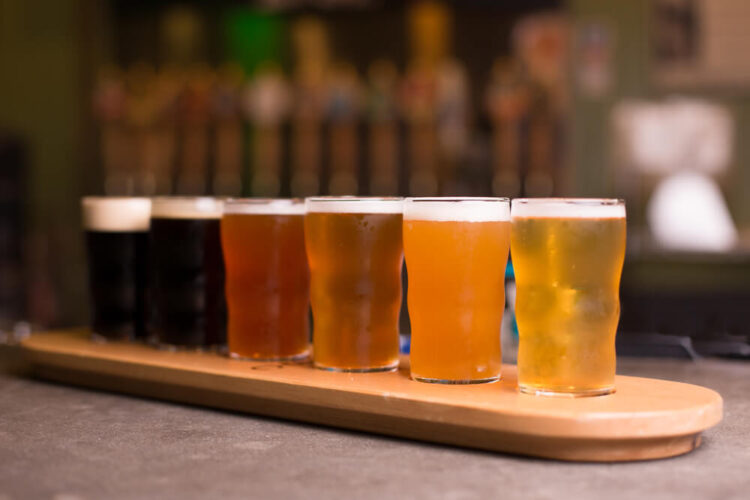 Flight of six beers ranging from dark stouts to red ales to lagers, served on  a plank of wood at a brewery.