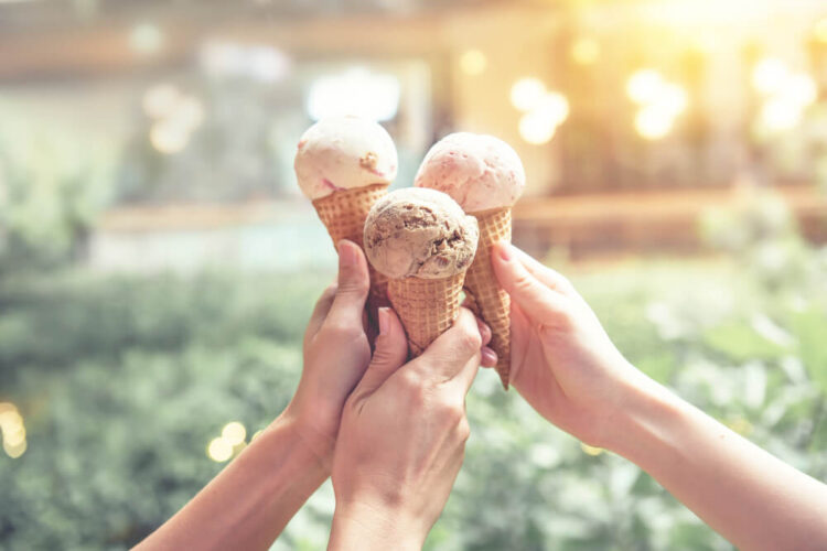 Three ice creams being held together in soft light with a park as the background.