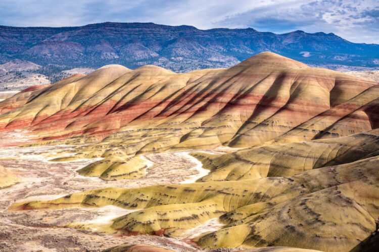 Colorful 'painted hills' in tones of brown, white, red, and yellow undulate on the landscape, with darker mountains in the background.