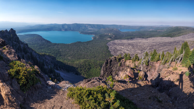 Newberry Caldera area from Paulina Peak, view of a deep turquoise lake far in the distance surrounded by trees and desert looking landscape.