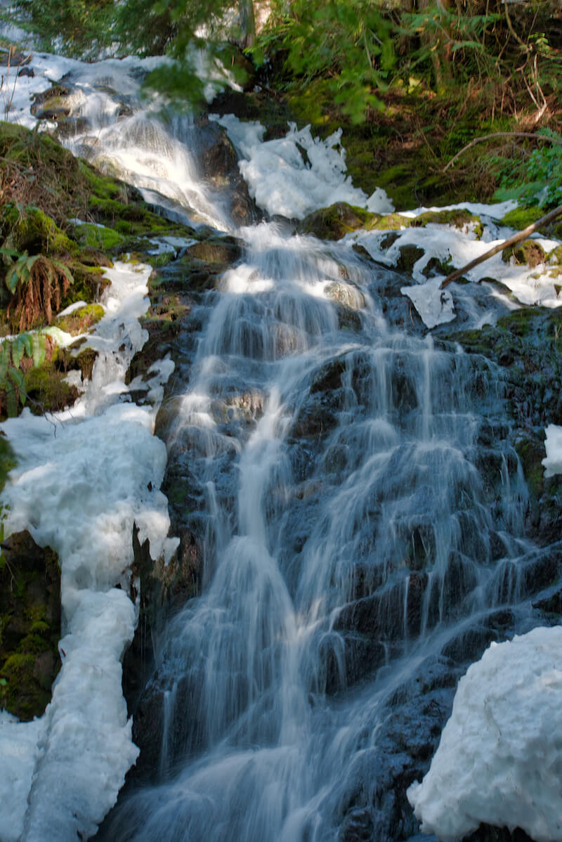 Melted snow on each side of the waterfall, which is flowing over rocks, not far from Seattle but requiring a hike to reach it.