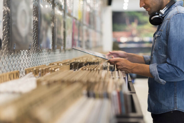 Hipster man in denim shirt with large  headphones around his neck looking for vinyl records in a vinyl shop in Eugene Oregon.